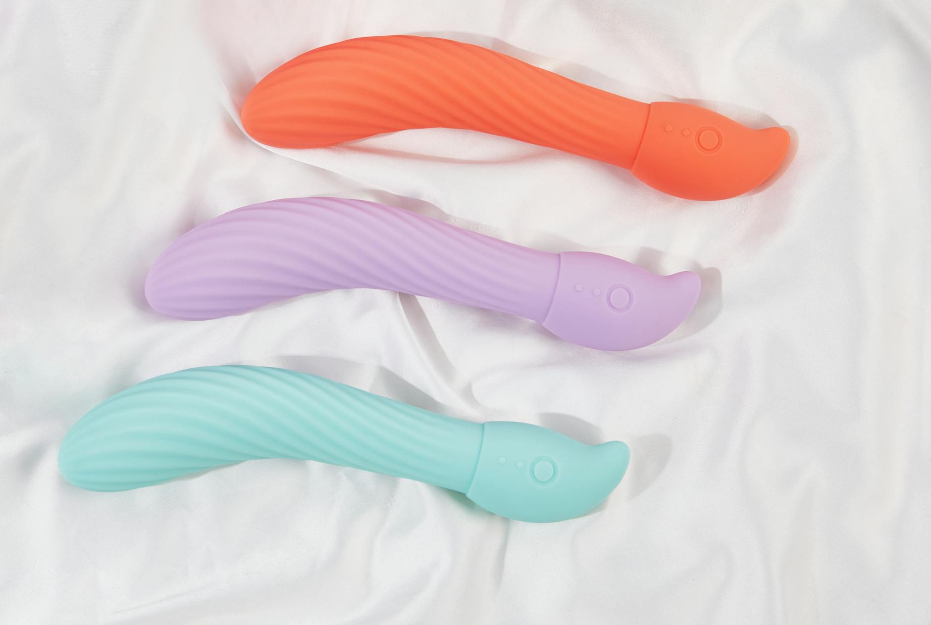 Three colorful clitoral vibrators arranged on white fabric, showing smooth texture and design details.