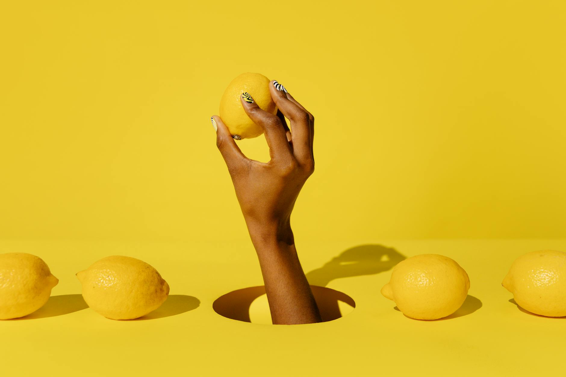 Hand holding a lemon against a vivid yellow background, symbolizing the fresh, natural sensation of clitoral stimulation