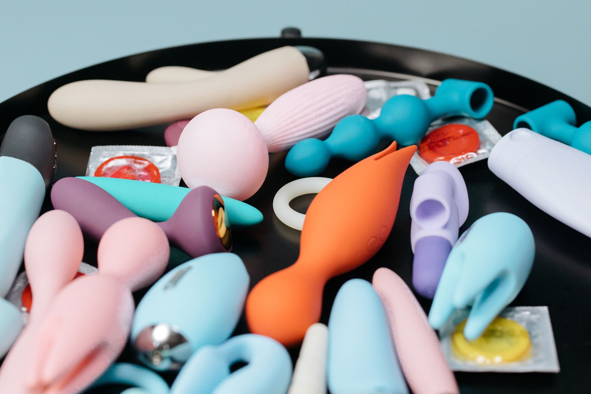 Vibrant collection of colorful clitoral vibrators and sex toys arranged on a bright yellow surface