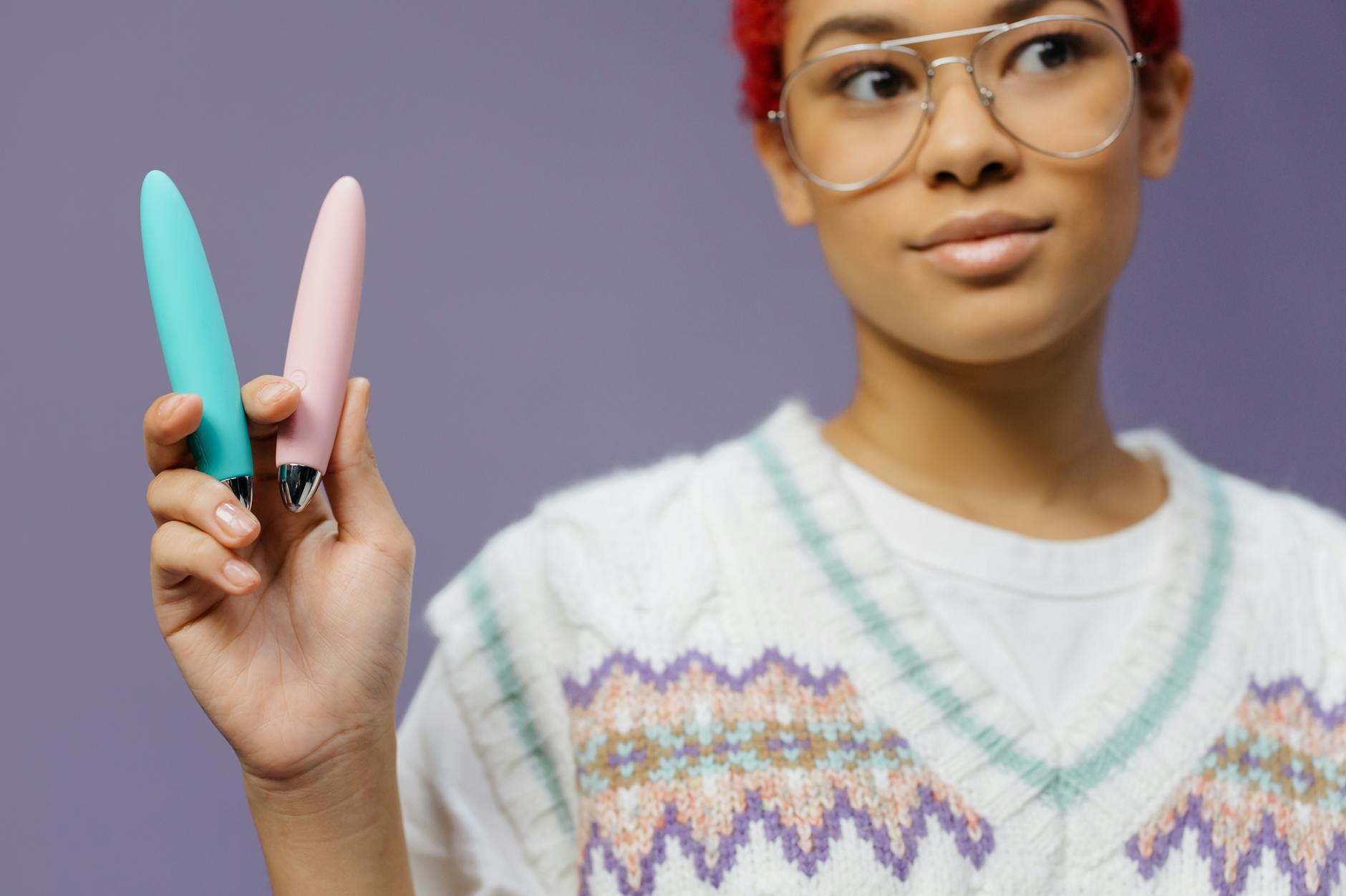 A woman holds two colorful vibrators against a purple background, representing pleasure restoration tools.